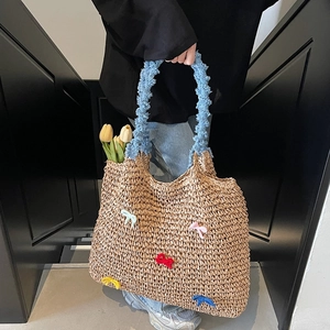Straw tote bag with colorful knitted bows and a blue plush handle on a minimal backdrop