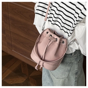 Sac seau rose à cordon avec texture tissée porté par un mannequin sur fond de bois