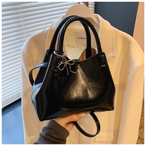 Detail of black glossy tote bag featuring a metallic beaded bow charm and dual straps