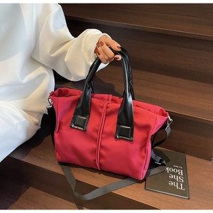 Detail of red nylon tote bag with black handles and detachable strap on wooden steps