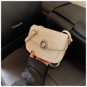 Detail of cream leather saddle bag with silver horseshoe buckle against a dark background