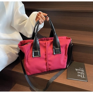 Magenta nylon tote bag with black leather handles and shoulder strap on wooden steps