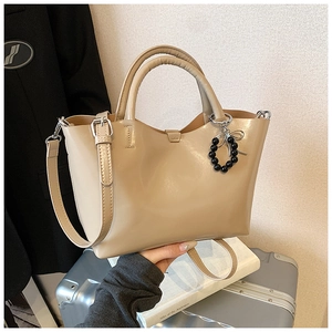 Close-up of beige glossy leather tote bag with black bead bow charm and silver hardware