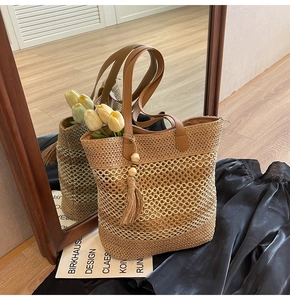 Detail of straw woven tote bag with hollow mesh pattern and leather handle and tassel