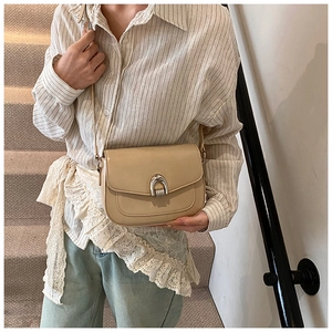 Detailed view of beige saddle bag with silver horseshoe buckle and matte leather texture