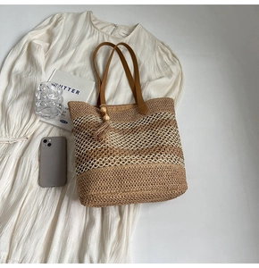 Detail of hand-woven straw tote with leather handles and decorative tassel on a dress