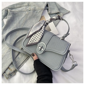 Detail of square handbag with woven texture, metal lock, and silk scarf handle