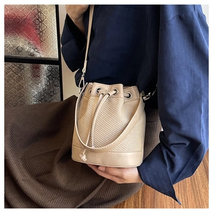 Détail d'un sac seau beige en paille tressée avec garniture en cuir brun et cordon serré