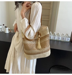 Detail of woven straw tote bag featuring leather straps and decorative tassel with wooden beads