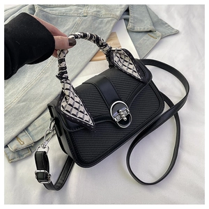 Detail of square handbag with woven texture, metal lock and silk scarf handle decoration