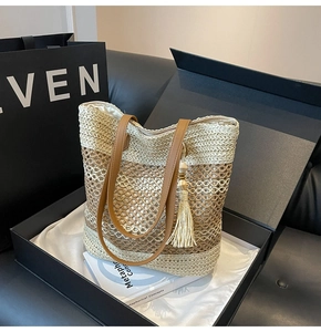 Close-up of woven straw tote bag with brown leather straps and stylish beige tassel charm