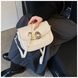 Detail of a beige leather saddle bag with horse-shoe buckle worn with a black blazer