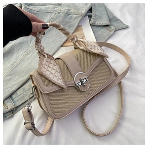 Detail of beige woven handbag featuring a silk scarf-wrapped handle and silver clasp