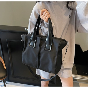 Detail of black tote bag featuring nylon body, leather handles and adjustable strap