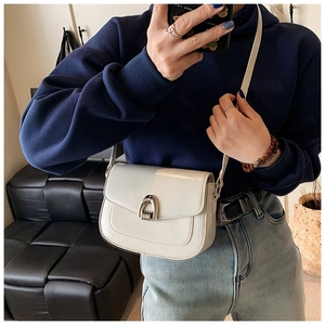 Detail of a creamy white saddle bag with a silver horseshoe buckle and leather strap