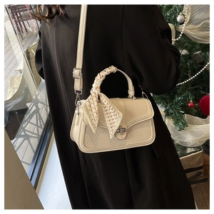 Detail of cream crossbody bag with woven texture and silk scarf handle on model