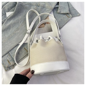 Détail d'un sac seau tissé en paille crème avec des finitions en cuir blanc lisse et chic