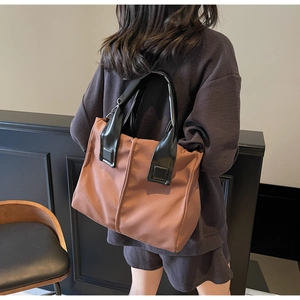 Rear view of a model carrying a brown tote bag with black handles in a casual street setting