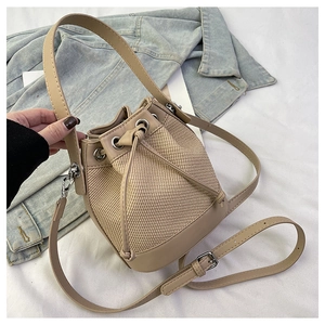 Détail d'un sac seau beige tissé avec bordure en cuir et bandoulière réglable pratique