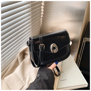Detail of a black leather saddle bag featuring a polished silver horseshoe buckle closure