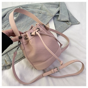 Détail d'un sac seau rose tressé avec bordure en cuir lisse et boucles en métal argenté brillant