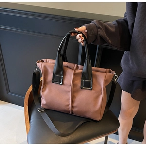 Detail of a brown nylon tote bag with black handles and silver metal hardware