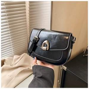 Detail of a black leather saddle bag featuring a stylish golden horseshoe metal buckle