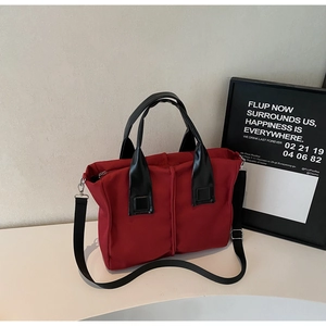 Close-up of red canvas handbag with black leather handles and adjustable shoulder strap