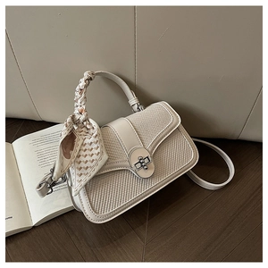 Detail of a beige patchwork handbag with woven texture, metal lock, and silk scarf handle
