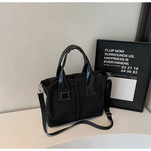 Detail of minimalist black nylon tote bag with leather handles and detachable canvas strap