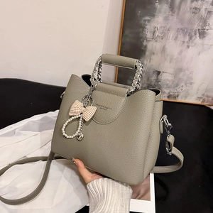 Green leather tote handbag with metal chain handle and pearl bow charm in high texture