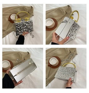 Detail of silver pleated evening clutch with golden dragon head handle and chain strap