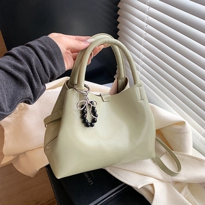 Green leather handbag with beaded bow charm shown in a stylish lifestyle setting