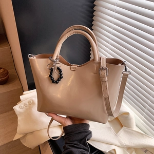 Elegant beige patent leather handbag with bow charm and detachable shoulder strap