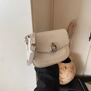 Chic beige saddle bag with silver buckle held in a minimalist warm indoor setting
