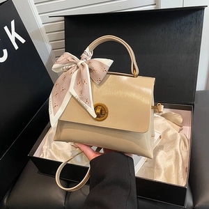 Detail of beige crossbody bag with silk scarf on handle and vintage metal twist lock