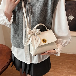 Detail of off-white crossbody bag with gold buckle and decorative floral bow scarf