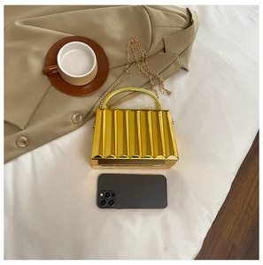 Detail of gold hard-shell evening bag with vertical pleated texture and metal handles