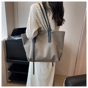 Détail du grand sac cabas taupe avec anses noires porté par une personne au bureau