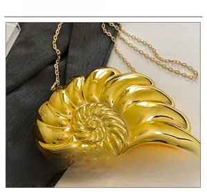Detail of a golden shell-shaped clutch bag with spiral texture and metal chain strap