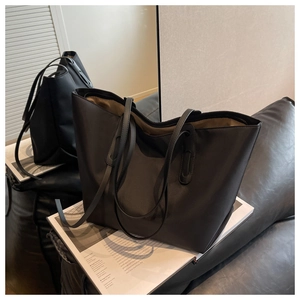 Grand sac cabas noir minimaliste avec de longues anses posé sur un magazine ouvert