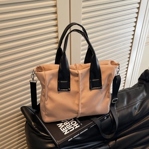 Chic beige crossbody tote with black handles and woven strap on a book display