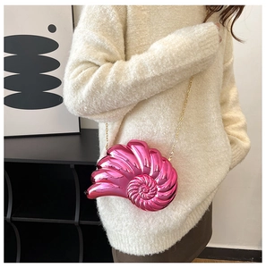 Detail of rose red metallic nautilus seashell bag with gold chain strap on a model
