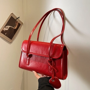 Detail of red glossy faux leather shoulder bag with matching heart pendant and double straps