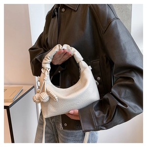 Detail der cremeweißen Hobo-Tasche mit Litschistruktur, Falten-Griff und Knoten-Anhänger