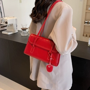 Detail of red glossy leather shoulder bag with heart pendant worn on beige blazer