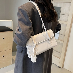 Detail of a creamy white glossy leather underarm bag worn with a grey blazer