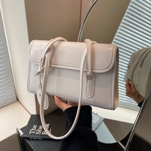 Detail of cream white faux leather shoulder bag featuring long straps and a round pendant