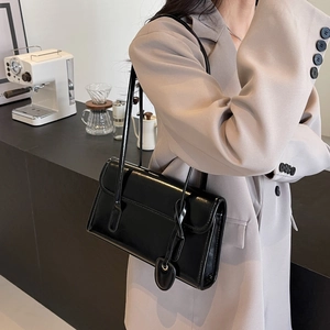 Detail of a black patent leather shoulder bag with a heart pendant in a chic cafe setting