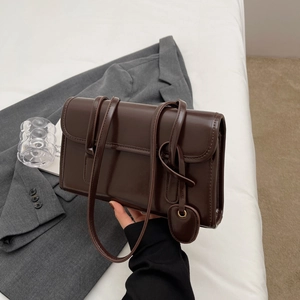 Detail of dark brown glossy shoulder bag with heart pendant held by hand in soft light
